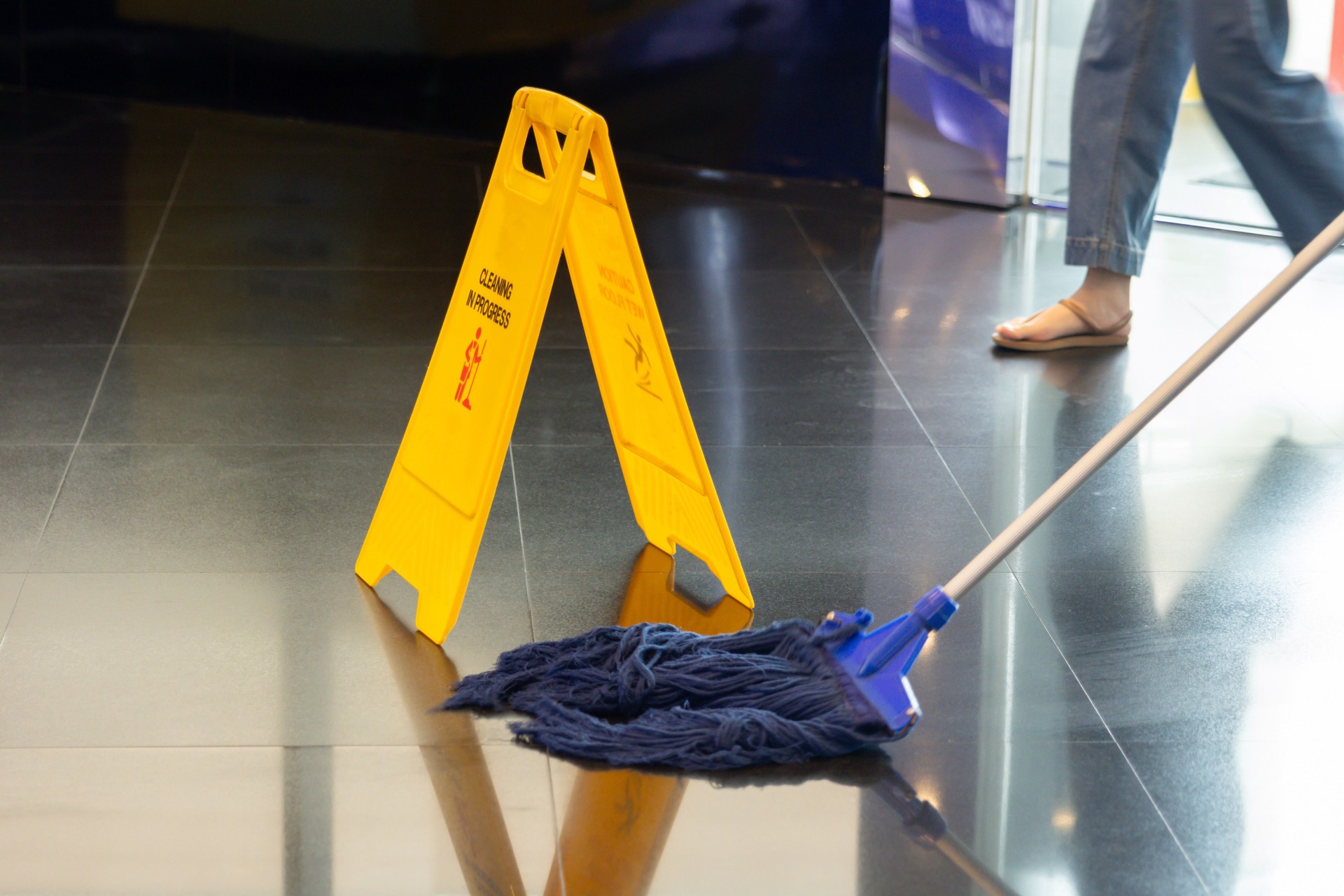 A yellow sign with the word "Caution" on it is on the floor. mop is cleaning the office floor.